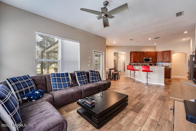 living room with ceiling fan, light hardwood / wood-style flooring, and a textured ceiling