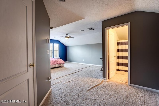 unfurnished bedroom featuring ensuite bath, vaulted ceiling, a textured ceiling, carpet floors, and ceiling fan