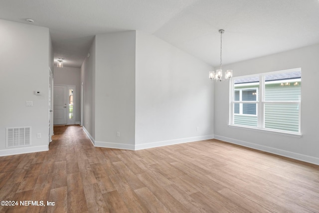 spare room featuring light wood-type flooring, lofted ceiling, and a notable chandelier