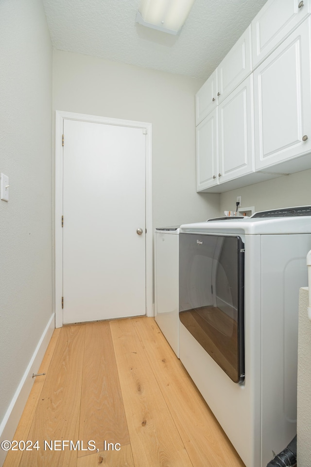 washroom featuring a textured ceiling, light hardwood / wood-style flooring, washing machine and dryer, and cabinets