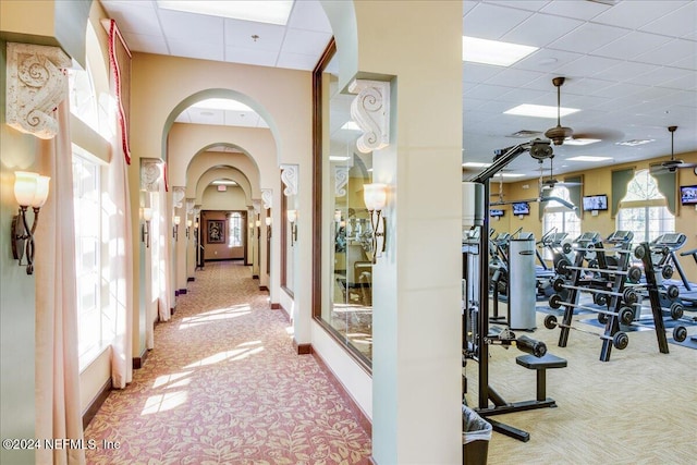 exercise room with a drop ceiling, light colored carpet, and ceiling fan