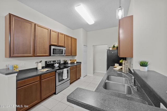 kitchen with a textured ceiling, sink, light tile patterned flooring, appliances with stainless steel finishes, and decorative light fixtures