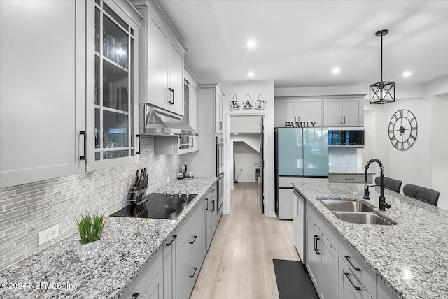 kitchen with tasteful backsplash, light stone countertops, hanging light fixtures, sink, and light hardwood / wood-style floors