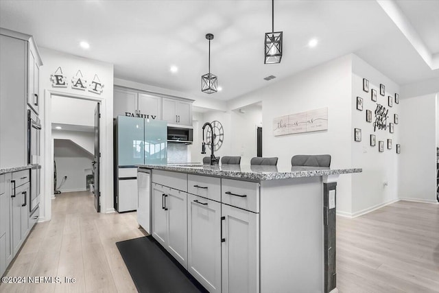 kitchen with gray cabinets, light wood-type flooring, hanging light fixtures, and an island with sink