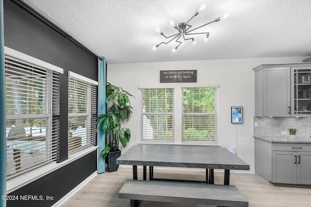 dining room with light wood-type flooring, a textured ceiling, and a notable chandelier