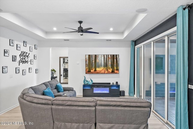 living room with ceiling fan, a tray ceiling, and light hardwood / wood-style floors