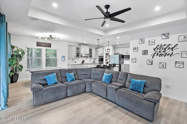 living room with light hardwood / wood-style floors, ceiling fan, and a raised ceiling