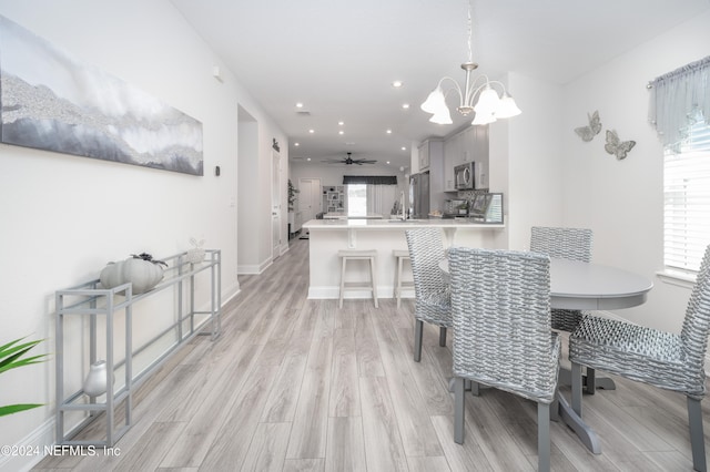 dining space featuring ceiling fan with notable chandelier and light wood-type flooring