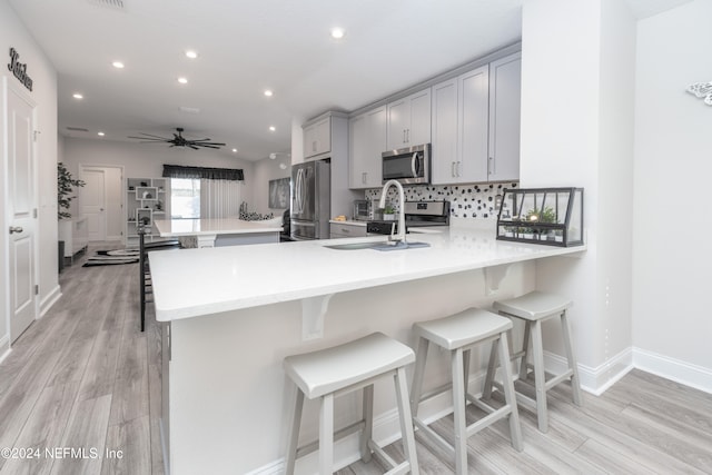 kitchen featuring kitchen peninsula, appliances with stainless steel finishes, a breakfast bar, and light hardwood / wood-style flooring