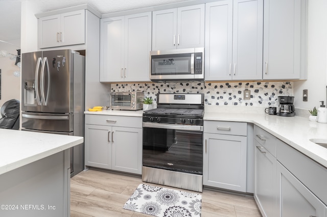 kitchen with light wood-type flooring, light stone countertops, decorative backsplash, and appliances with stainless steel finishes