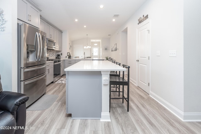 kitchen with a kitchen island, appliances with stainless steel finishes, pendant lighting, a breakfast bar, and light hardwood / wood-style flooring