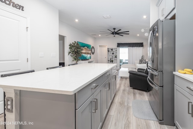 kitchen featuring gray cabinetry, a kitchen island, light wood-type flooring, stainless steel refrigerator, and lofted ceiling