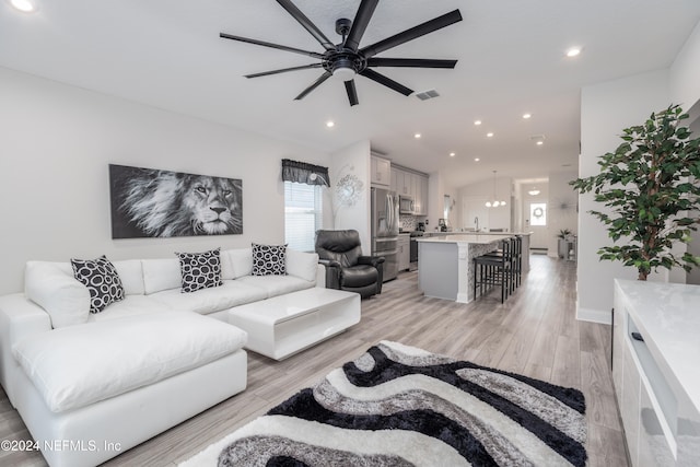 living room with light hardwood / wood-style floors, ceiling fan with notable chandelier, and sink