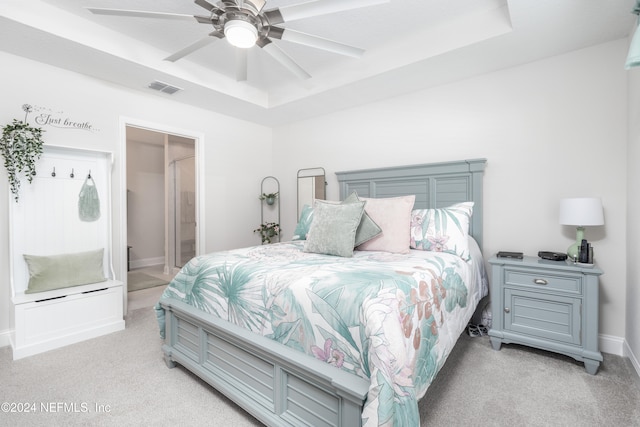 carpeted bedroom with a tray ceiling, ceiling fan, and ensuite bathroom