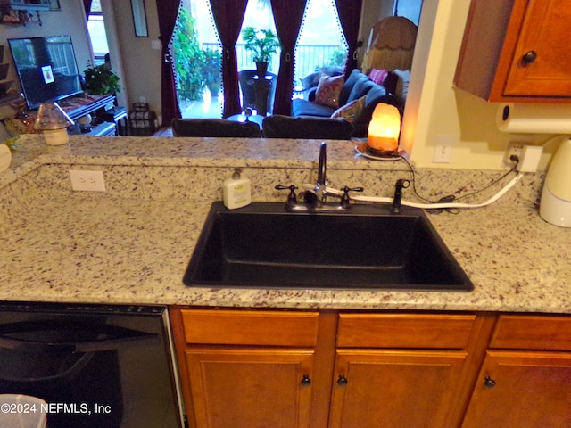 kitchen featuring dishwasher, light stone countertops, and sink