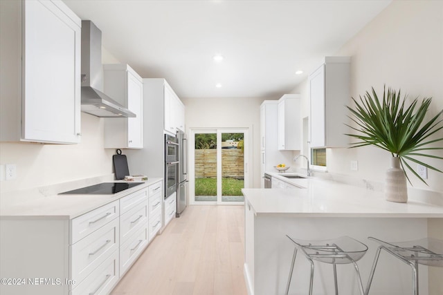 kitchen with kitchen peninsula, wall chimney exhaust hood, sink, light hardwood / wood-style flooring, and white cabinets