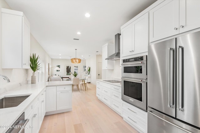 kitchen featuring kitchen peninsula, stainless steel appliances, wall chimney range hood, light hardwood / wood-style flooring, and white cabinetry