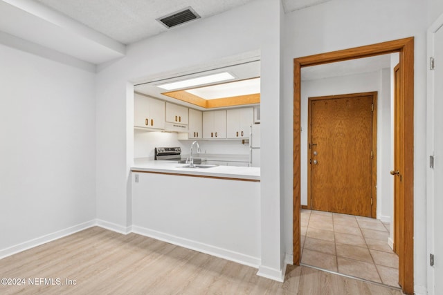 kitchen with stainless steel range with electric stovetop, white cabinets, sink, light hardwood / wood-style flooring, and white fridge