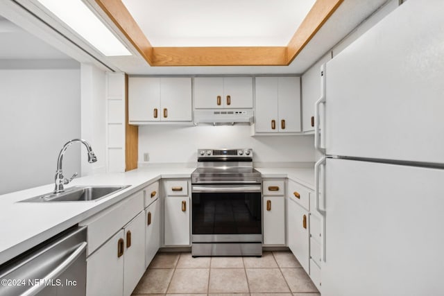 kitchen featuring appliances with stainless steel finishes, a tray ceiling, sink, white cabinetry, and light tile patterned flooring