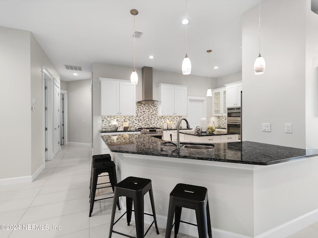 kitchen featuring white cabinetry, decorative light fixtures, sink, and wall chimney range hood