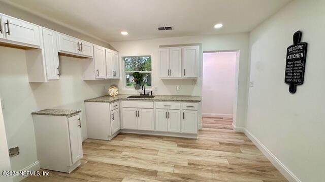 kitchen featuring stone countertops, white cabinetry, sink, and light hardwood / wood-style flooring