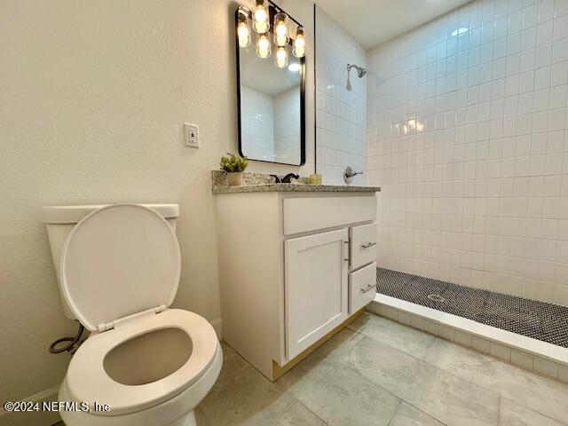 bathroom featuring toilet, vanity, tile patterned flooring, and a tile shower