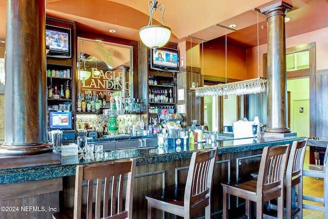 bar with hardwood / wood-style flooring, ornate columns, and decorative light fixtures