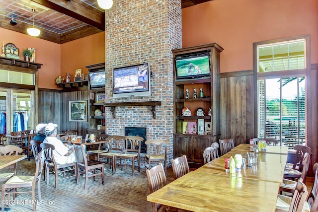 dining area featuring hardwood / wood-style floors, a high ceiling, beamed ceiling, and a brick fireplace