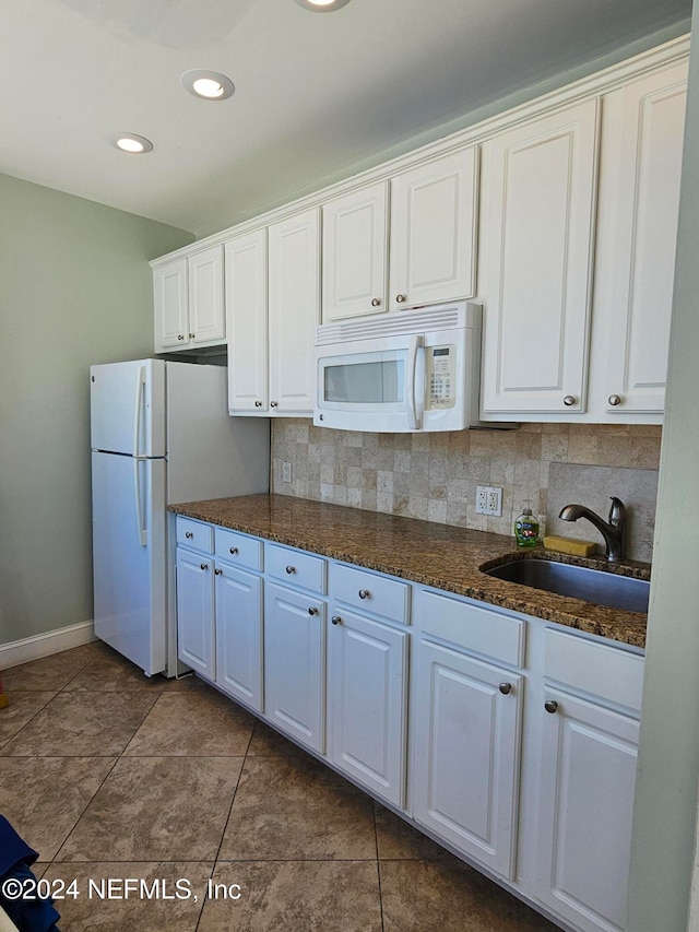 kitchen with dark tile patterned flooring, sink, backsplash, white cabinetry, and white appliances