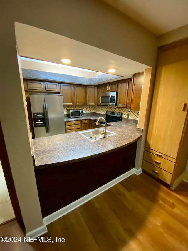 kitchen featuring hardwood / wood-style flooring, sink, kitchen peninsula, appliances with stainless steel finishes, and tasteful backsplash