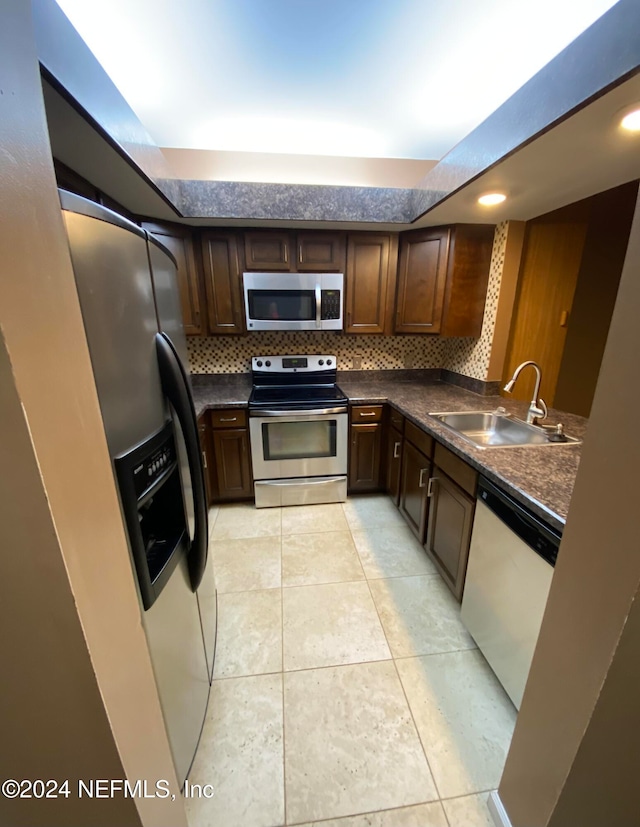 kitchen with stainless steel appliances, backsplash, dark brown cabinets, light tile patterned floors, and sink