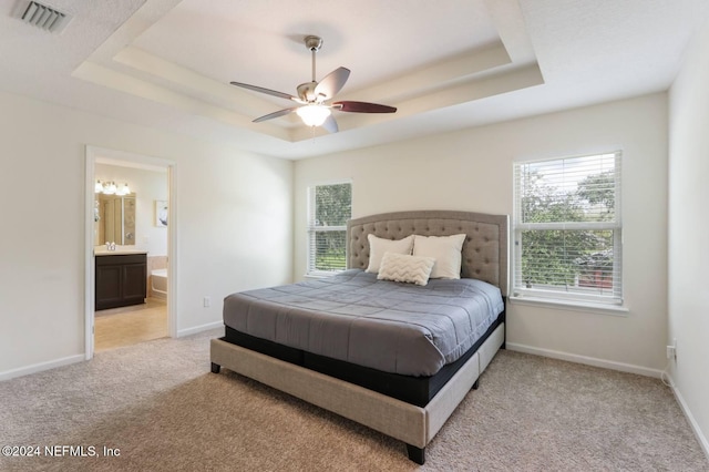 bedroom with ensuite bathroom, light carpet, ceiling fan, and a tray ceiling