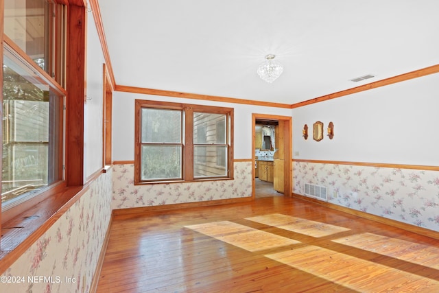 empty room with plenty of natural light, wood-type flooring, crown molding, and an inviting chandelier