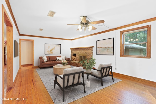 living room featuring ornamental molding, light wood-type flooring, ceiling fan, and a brick fireplace