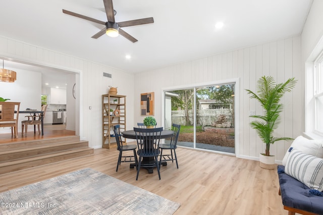 dining area with wooden walls, ceiling fan, and light hardwood / wood-style flooring