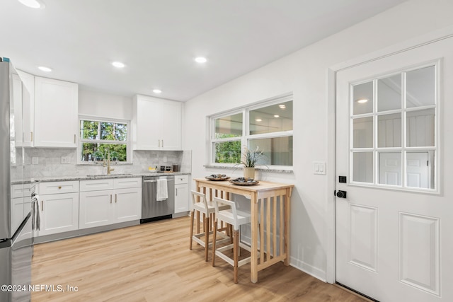 kitchen featuring tasteful backsplash, white cabinetry, light wood-type flooring, sink, and dishwasher