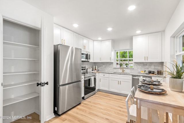 kitchen featuring light hardwood / wood-style floors, light stone counters, white cabinets, decorative backsplash, and appliances with stainless steel finishes