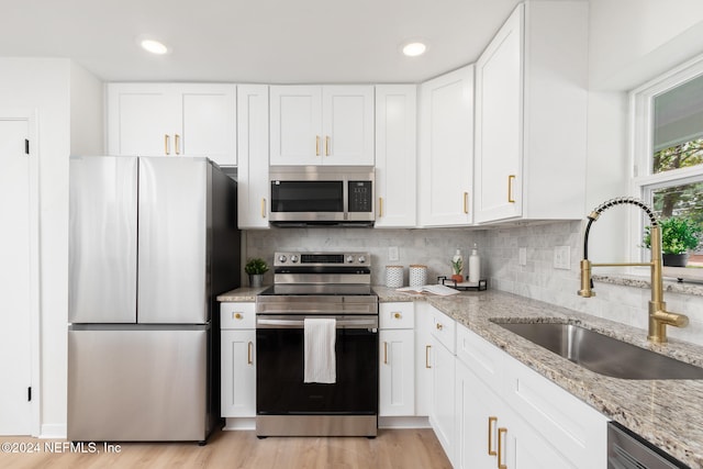 kitchen with stainless steel appliances, sink, light stone countertops, white cabinetry, and light wood-type flooring