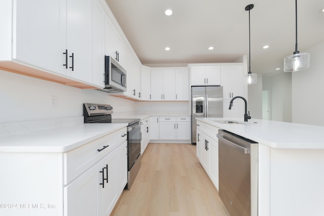 kitchen with white cabinets, sink, an island with sink, appliances with stainless steel finishes, and decorative light fixtures