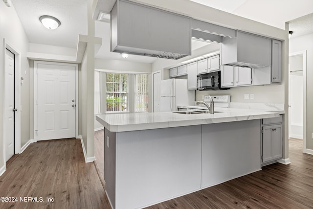 kitchen with dark wood-type flooring, gray cabinetry, kitchen peninsula, and white fridge