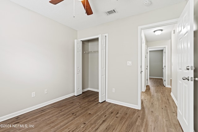 unfurnished bedroom with a textured ceiling, light hardwood / wood-style flooring, ceiling fan, and a closet