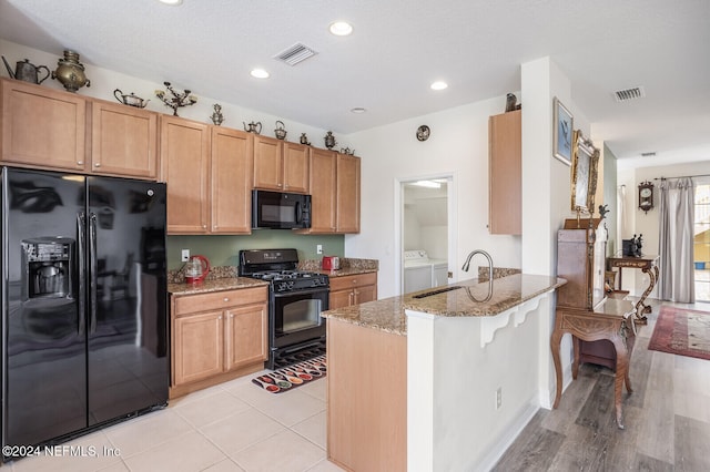 kitchen featuring black appliances, light hardwood / wood-style flooring, light stone countertops, kitchen peninsula, and washing machine and clothes dryer