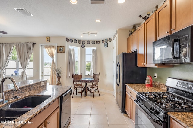 kitchen with a textured ceiling, sink, black appliances, and stone countertops