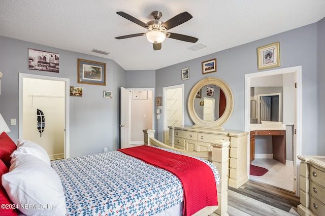 bedroom with hardwood / wood-style floors, ensuite bathroom, ceiling fan, a spacious closet, and a textured ceiling