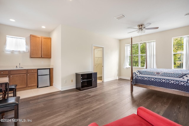 bedroom with sink, light hardwood / wood-style flooring, ceiling fan, stainless steel fridge, and connected bathroom