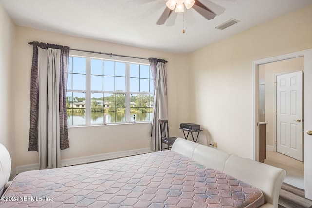 bedroom with ceiling fan, light hardwood / wood-style flooring, and a water view