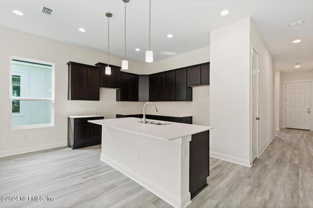 kitchen with light wood-type flooring, a center island with sink, hanging light fixtures, and sink