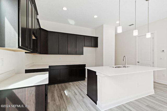 kitchen featuring a center island with sink, sink, decorative light fixtures, and light hardwood / wood-style flooring