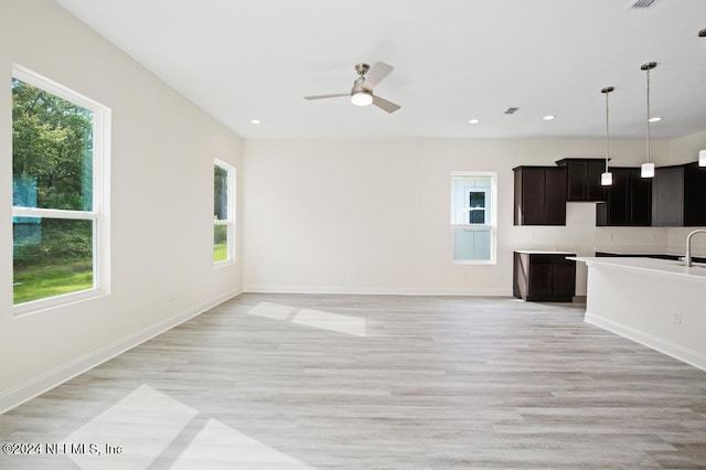 unfurnished living room with light wood-type flooring, sink, ceiling fan, and a healthy amount of sunlight