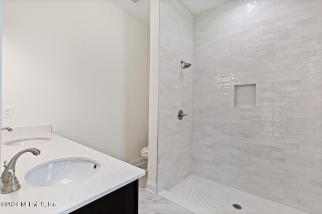 bathroom with a tile shower, vanity, and toilet